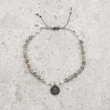 Bracelet made of Labradorite and Moonstone semi-precious gemstone beads strung with tiny silver beads in a pattern.  There is a charm in the middle of the gemstone and silver bracelet that has a lotus flower on it