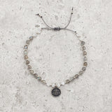 Bracelet made of Labradorite and Moonstone semi-precious gemstone beads strung with tiny silver beads in a pattern.  There is a charm in the middle of the gemstone and silver bracelet that has a lotus flower on it 
