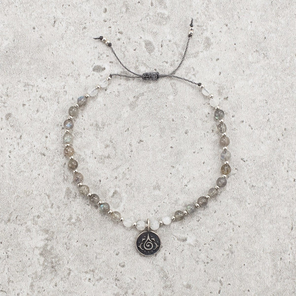 Bracelet made of Labradorite and Moonstone semi-precious gemstone beads strung with tiny silver beads in a pattern.  There is a charm in the middle of the gemstone and silver bracelet that has a lotus flower on it 